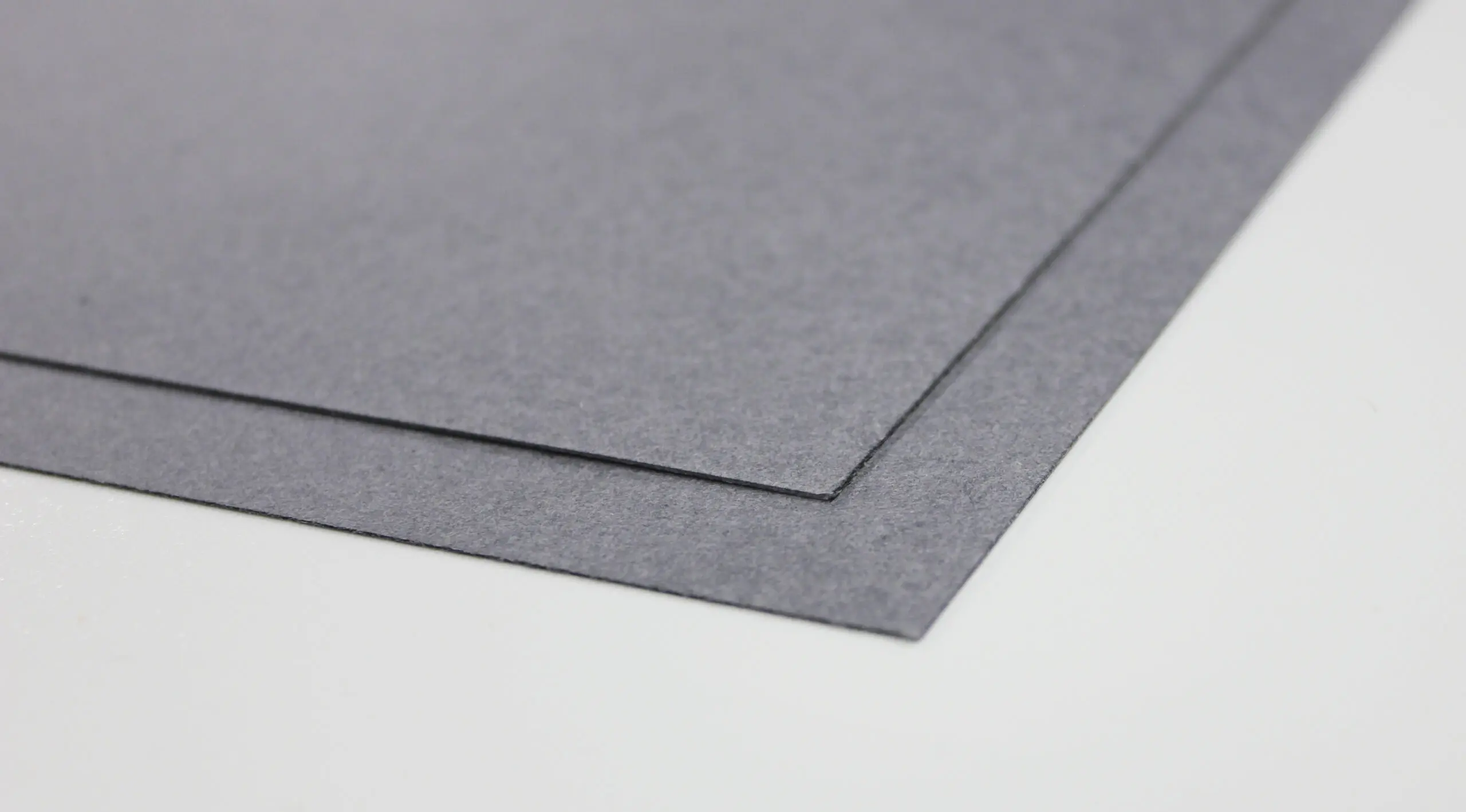 Two gray rectangular sheets of material are layered and angled on a white surface.